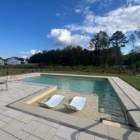 Modern Desjoyaux pool with built-in tanning ledge and lounge chairs in a spacious backyard — request your custom pool design today